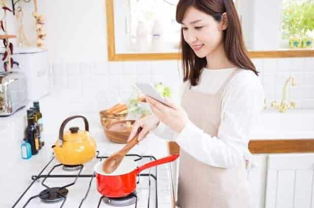 Young asian woman cooking while referring to her phone 
